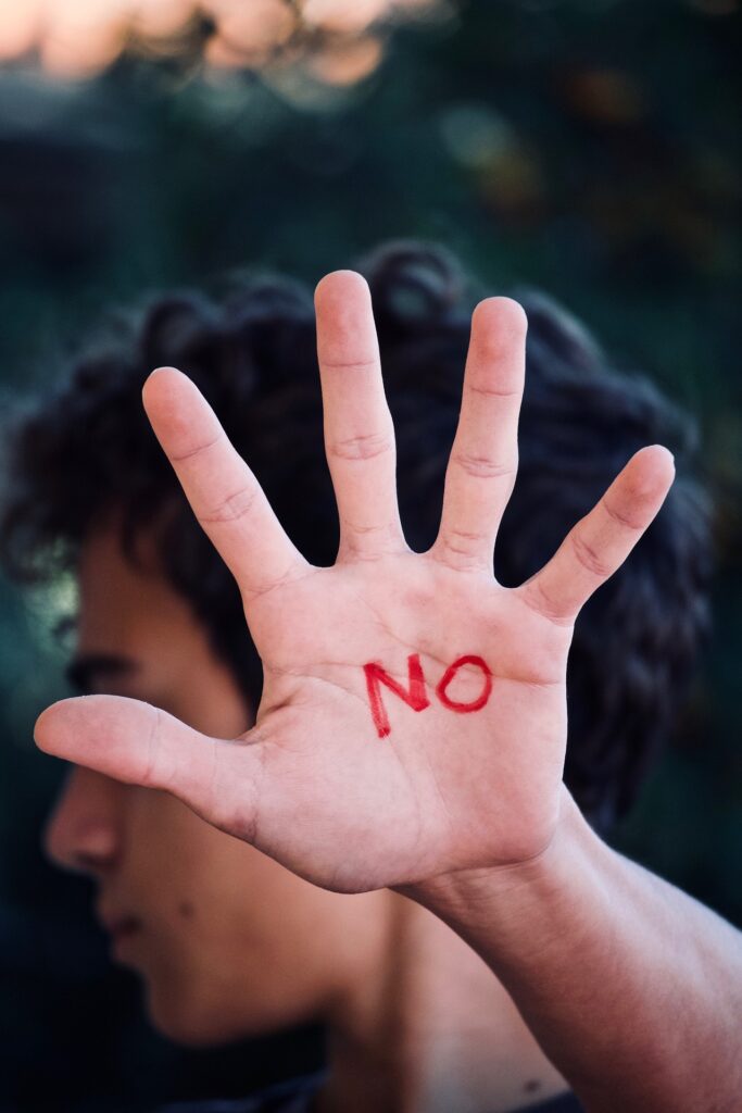 Person holding the palm of their hand up with writing in red lettering "NO"